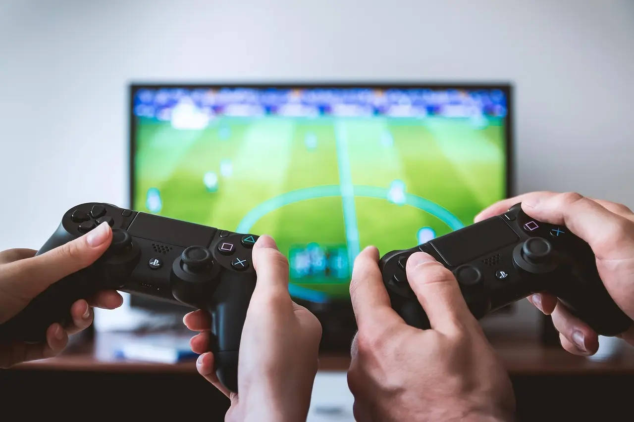 Hænder med controllere foran fodboldspil